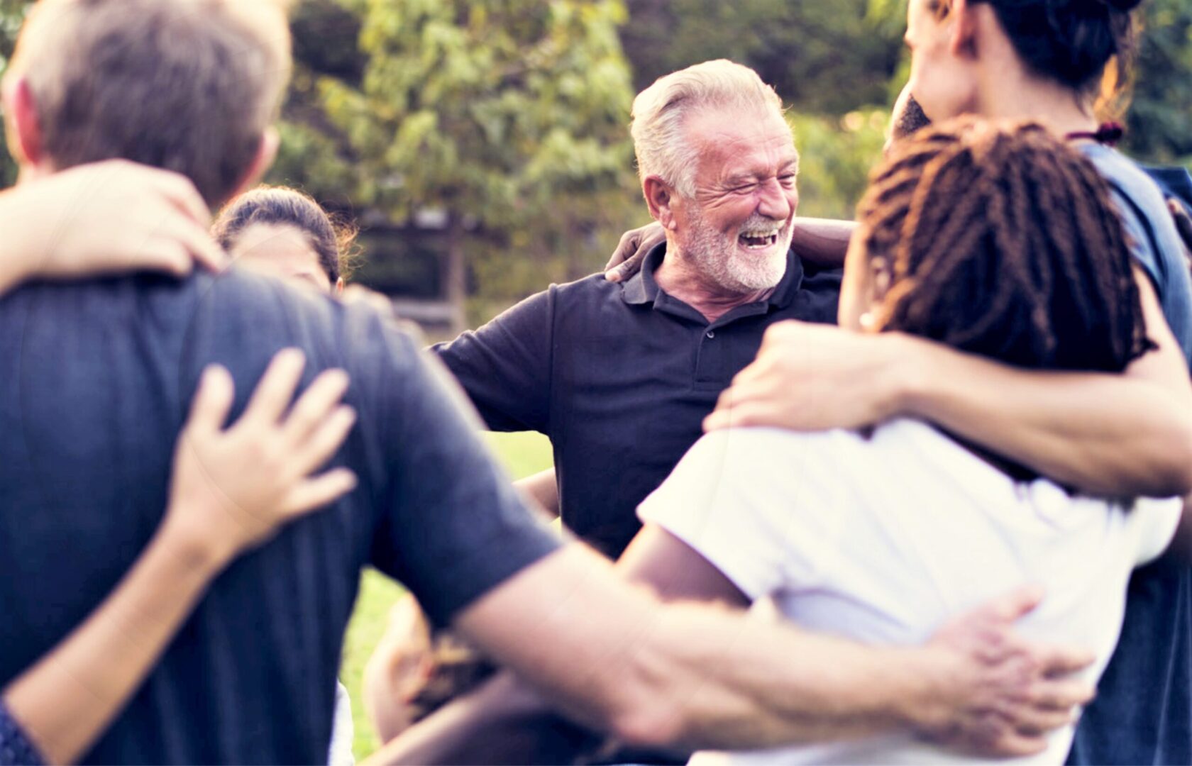 Group of people embracing and smiling outdoors.