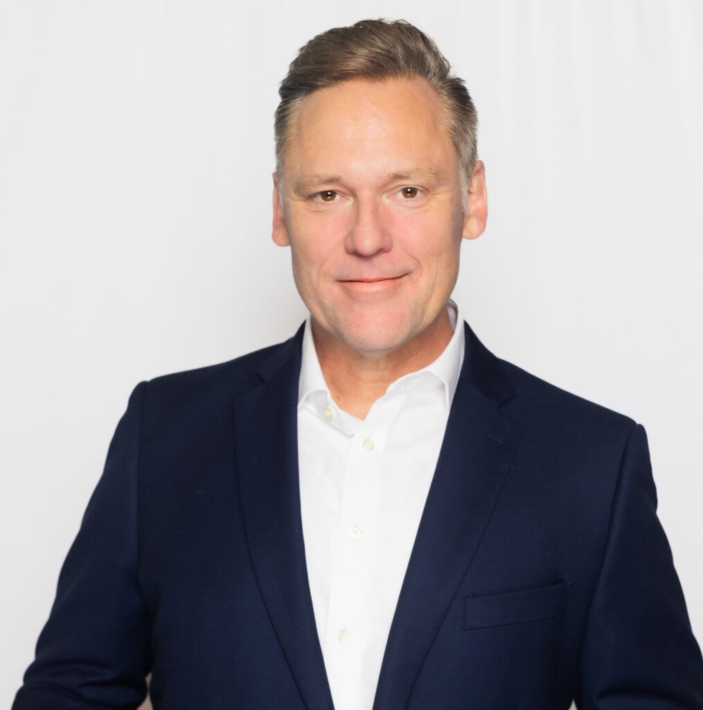 Professional man in a navy blazer and white shirt smiles confidently.